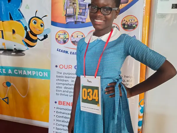 A smiling HEWIS spelling-bee participant wearing a competitor badge